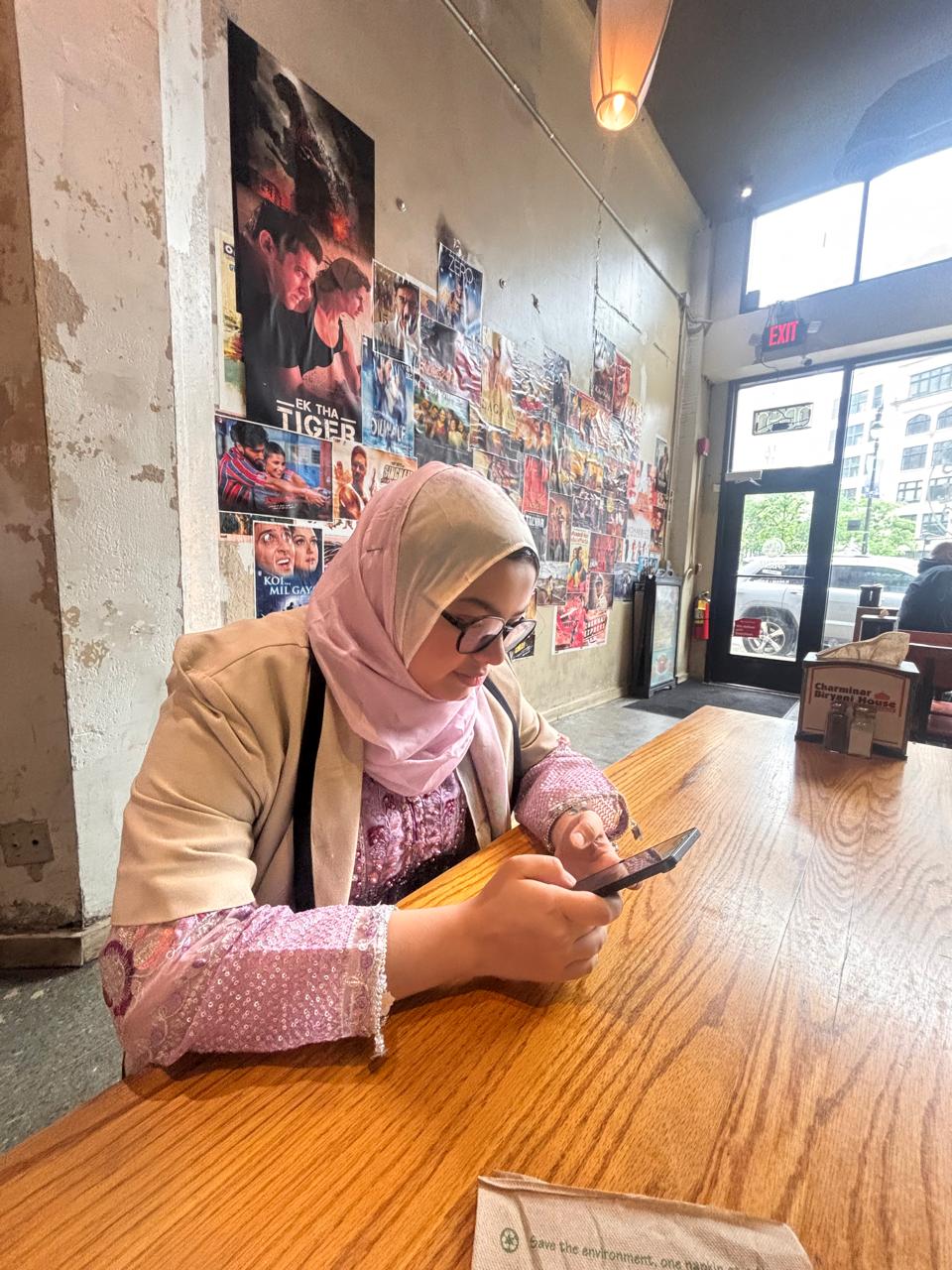 The researcher sits at a wooden cafe table holding a phone