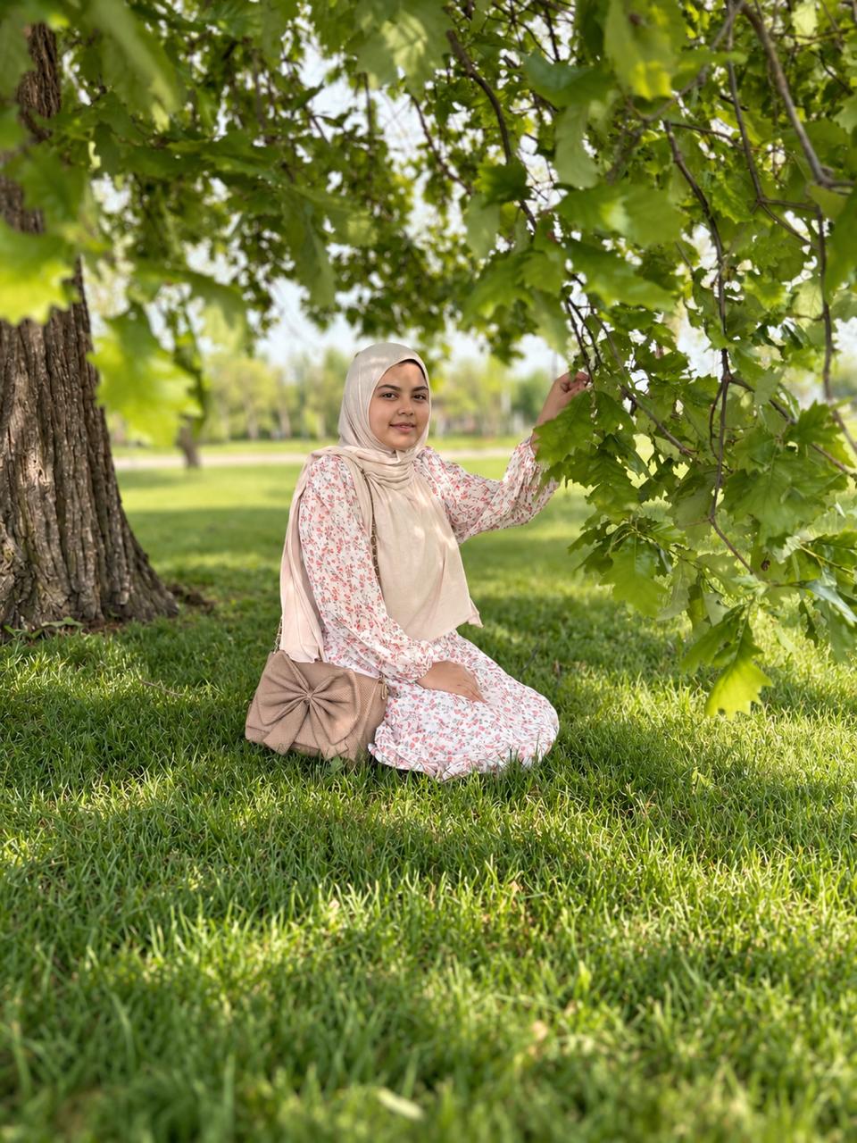 The researcher kneels on grass beneath green leaves
