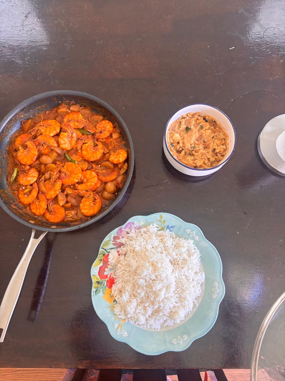 A pan of shrimp, a bowl of vegetables, and a plate of rice on a table